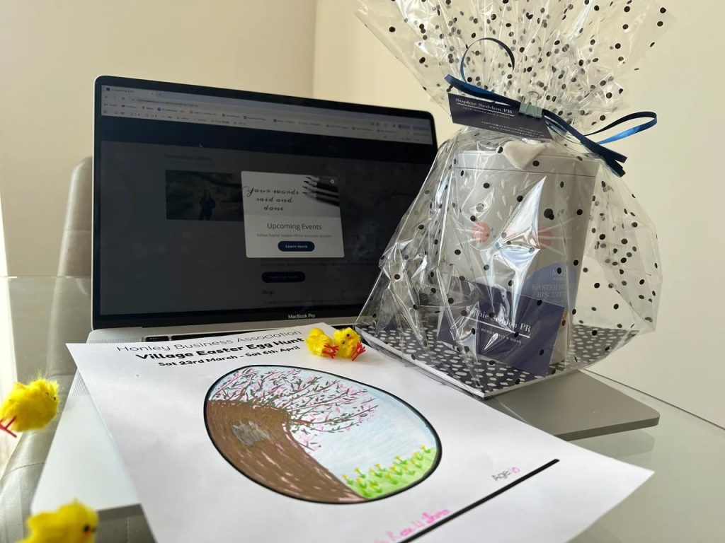 Laptop with Sophie Seddon PR's Easter Egg donation to Honley Business Association (HBA), her daughter's Easter drawing and decorative Easter chicks on a table.