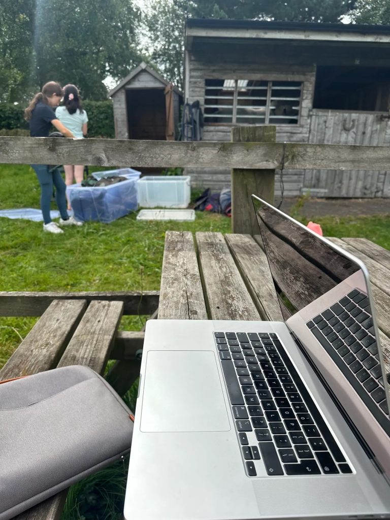 Sophie, of Sophie Seddon PR's two daughters sorting out their pony loan shed in a field while Sophie works at her laptop.