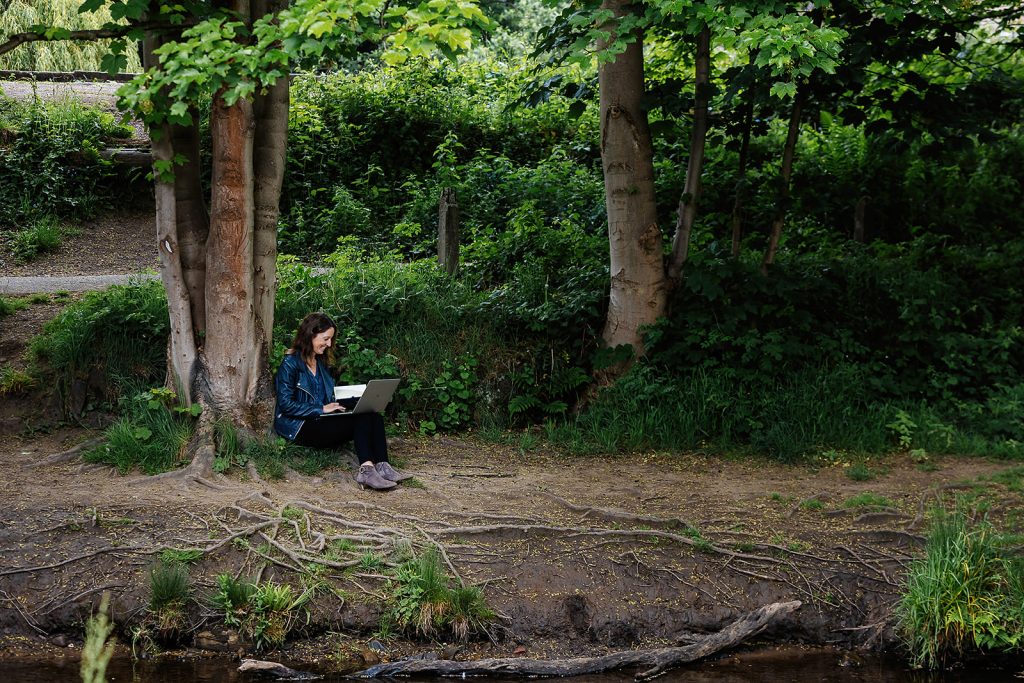 Sophie Seddon, of Sophie Seddon PR, working outside. She is sat on the river bank in Madgale, Honley, with her notebook and pencil, writing in shorthand.