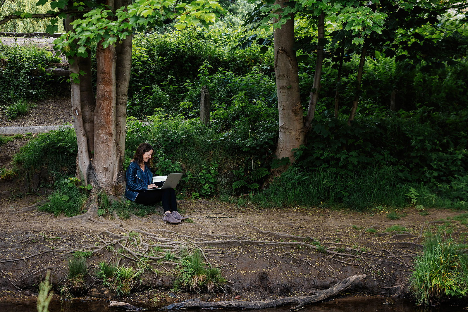 Sophie Seddon, of Sophie Seddon PR, working outside. She is sat on the river bank in Madgale, Honley, with her notebook and pencil, writing in shorthand.